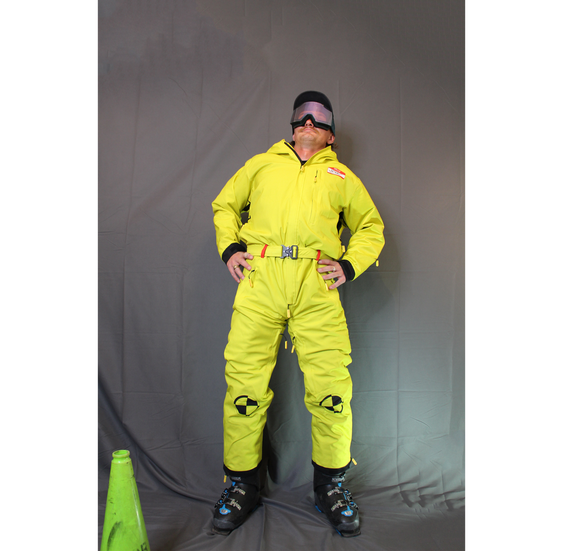Front view of a model wearing a bright yellow Shred Suit with goggles, belt, chest pocket, and boot buckles visible